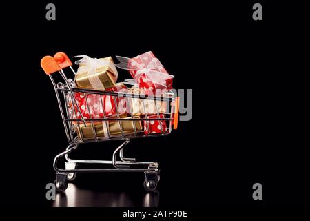 Shopping cart trolley full of colorful gift boxes on black background. Concept of shopping for christmas or black friday. Stock Photo