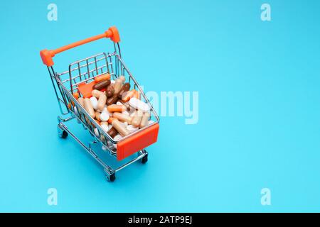 Shopping cart full of medical pills on blue background. Concept of drug consumption or abuse. Top view. Stock Photo