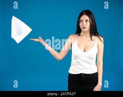 Pensive brunette girl throwing paper isolated on blue background. Stock Photo