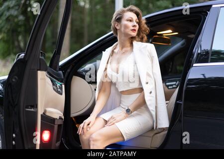 Dreamy well dressed woman sitting in car and looking away. Stock Photo