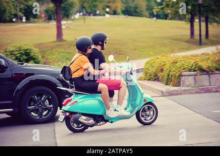 Montreal, Canada - June, 2018: Young couple with helmets having a ride on scooter in the city of Montreal, Canada. Stock Photo