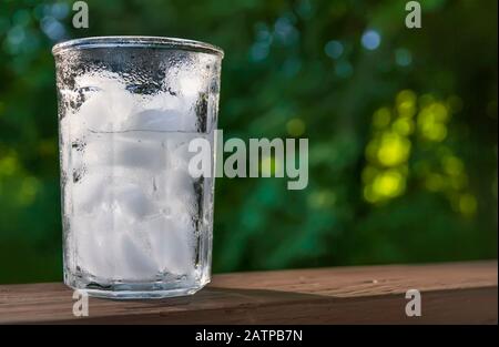 Glass of ice water on wooden deck railing Stock Photo