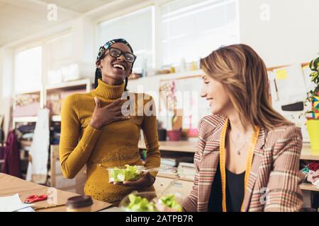 Two young entrepreneur women, or fashion designers working in atelier and making short breakfast break at work Stock Photo