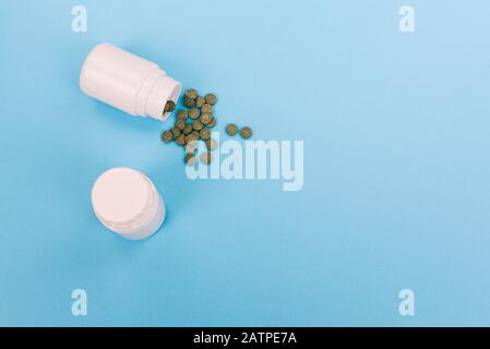 Green pills from a white bottle. Pills spilling out of a bottle on a blue background. Small white plastic jars with pills on a medical background Stock Photo