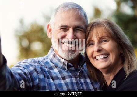A mature couple enjoying time together and taking a self-portrait while enjoying the sunset in a city park on a warm fall evening Stock Photo