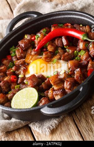 Sisig is a popular Filipino dish. It is composed of pork, chopped onion, and chicken liver close-up in a pan on the table. vertical Stock Photo