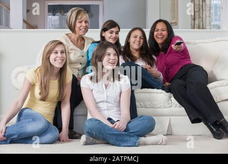 Two mothers watching television with four teenage girls Stock Photo