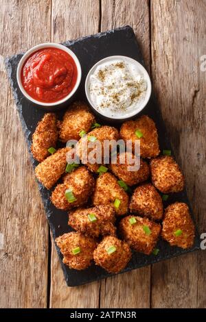 Deep-fried coconut breaded chicken with two sauces close-up on a slate board on a table. Vertical top view from above Stock Photo