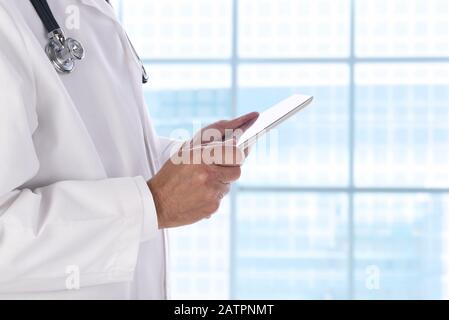 Closeup of a medical professional holding a tablet computer while standing in front of a large window in a modern medical facility. Stock Photo