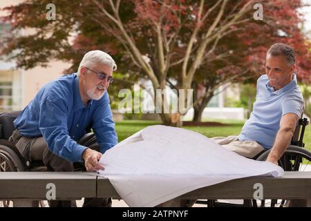 Men in wheelchairs sitting in an outdoor area looking at blueprints Stock Photo