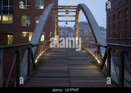 Metal and wooden industrial pedestrian bridge in old industrial area of Hamburg in the evening with lights on the metal structure. Hamburg, Germany Stock Photo