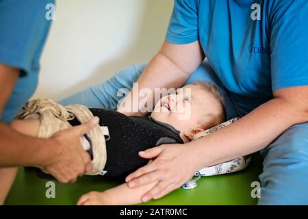 Portrait of a baby with cerebral palsy on physiotherapy in a children therapy center. Boy with disability has therapy by doing exercises. Little kid h Stock Photo