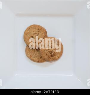 Who doesn't love cookies? Three round peanut butter cookies on a square white plate. Stock Photo