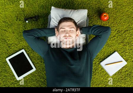 Student Resting Lying On Green Grass Carpet Among Belongings, Above-View Stock Photo