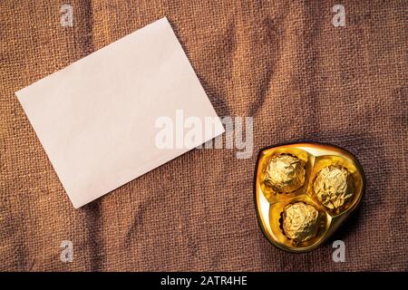Heart shape chocolate box with empty white card paper on a burlap for valentine's day concept. Romantic flat lay background for invitation, poster, gi Stock Photo