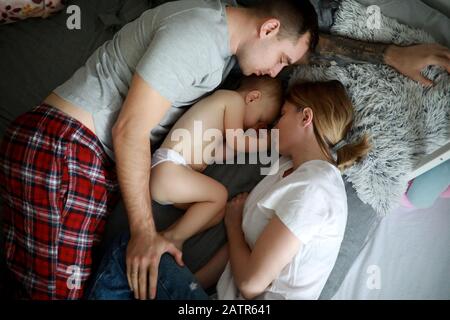 Family with baby sleeps together on the bed. Top view. Stock Photo