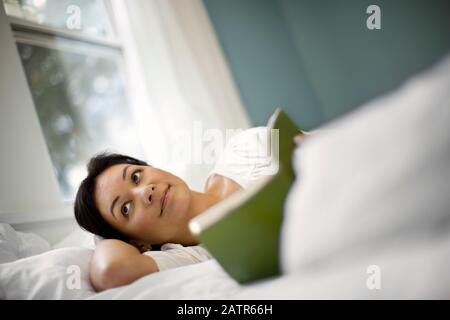 Content young woman lying in bed reading a book. Stock Photo
