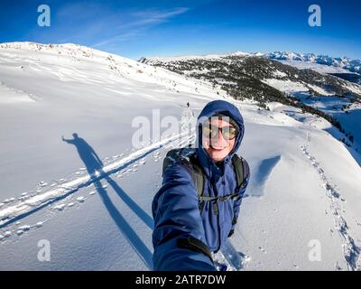 mountaineer smiling into the camera in the winter wonderland against beautiful mountain panorama. sunny, blue sky Stock Photo