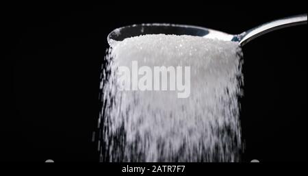 Sugar or Salt falling off spoon from a bowl at closeup Stock Photo