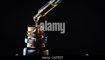 CBD Hemp oil, Hand holding droplet of Cannabis oil against black background. Alternative Medicine Stock Photo