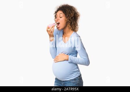 Pregnancy diet. Hungry afro expectant girl biting donut Stock Photo