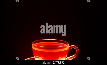 Close up of isolated transparent glass cup of brown coffee illuminated in red light, black background Stock Photo