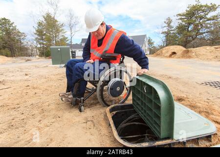 Man in wheelchair working on underground cables Stock Photo