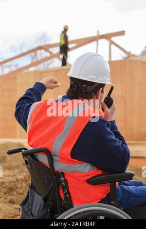 Man in a wheelchair uses a walkie talkie on a construction site Stock Photo