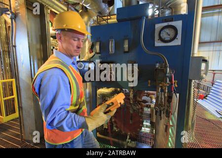 Worker wearing hard hat and reflective vest using equipment with gauges and monitors Stock Photo