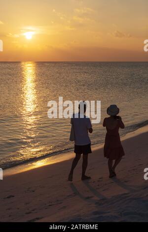 Couple on beach - a couple walking on a tropical beach watching the sunset over the Indian Ocean, the Maldives, Asia Stock Photo