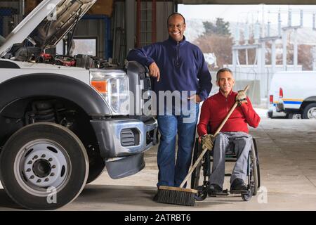 Vehicle mechanic and man in wheelchair with broom posing for a picture Stock Photo