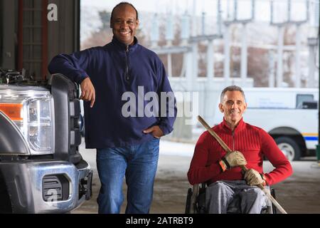 Vehicle mechanic and man in wheelchair with broom posing for a picture Stock Photo