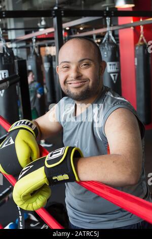 Young man with Down Syndrome wearing boxing gloves in a gym and smiling for the camera Stock Photo