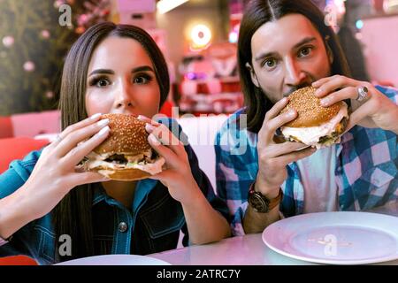 Starving people enjoys their yummy food in good cafe. Wearing casual clothing, checkered shirt and jeans. Beautiful girl with long brunette hair, make Stock Photo
