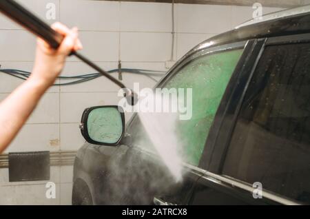 An employee of the car wash thoroughly washes conducts detaling and applies protective equipment to the body of an expensive car Stock Photo