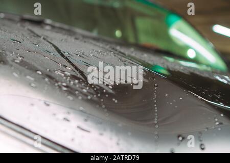 An employee of the car wash thoroughly washes conducts detaling and applies protective equipment to the body of an expensive car Stock Photo