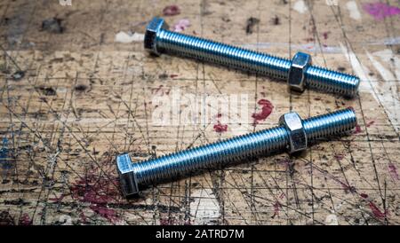 Bolts with metal hex nuts on  wooden workbench stained grunge textured surface. Muted colors effect, panoramic frame. Stock Photo