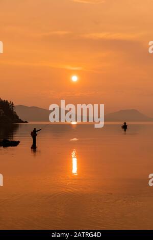 Silhouetted angler standing in the tranquil water fishing for king salmon at dusk; Alaska, United States of America Stock Photo