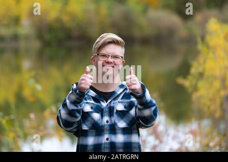 A young man with Down Syndrome giving a thumbs up in a city park on a warm fall evening: Edmonton, Alberta, Canada Stock Photo
