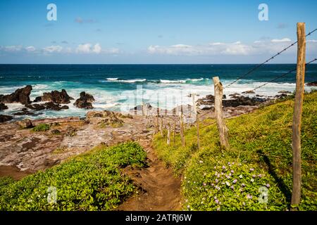 Ocean waves cresting and rollling into the rocky shoreline with a dirt path on a fenceline and clouds on the horizon as viewed from the Ho'okipa Lo... Stock Photo