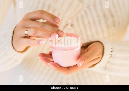 Woman holds natural white smooth cream. Cosmetic product and beauty skincare concept. Blank pink container. Close up with cream and female hands. Stock Photo