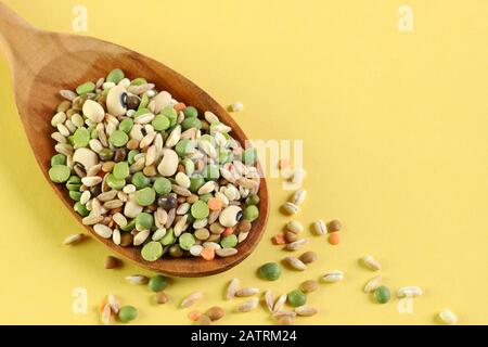 Mix of dried legumes in a wooden spoon isolated on yellow background. Top view. Stock Photo