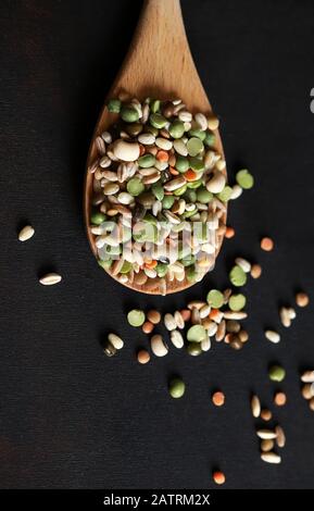 Mix of dried legumes in a wooden spoon isolated on dark background. Top view. Stock Photo