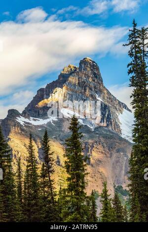 Mountain cliff peak dramatically lit by the sun with blue sky and clouds, Yoho National Park; Field, British Columbia, Canada Stock Photo