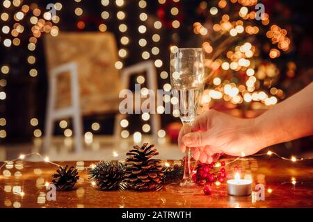 Spending Christmas holidays alone and drinking champagne alone, Holiday depression and alcoholism concept. Selective focus on hand with alcohol flute Stock Photo