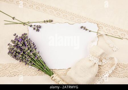 Top view of white empty sheet of paper with burned edges and surrounded by fresh lavender branches and scented dry lavender bag sachet on old page. Stock Photo