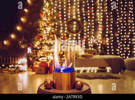 Selective focus on modern freestanding portable glass and copper metal fireplace burning bio ethanol gas on living room table with cozy Christmas eve Stock Photo