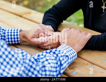 A mature couple praying together at a picnic table after spending some quality time discussing their faith; St. Albert, Alberta, Canada Stock Photo