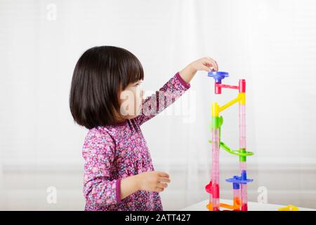 toddler girl play marble run game at gome agianst white background Stock Photo