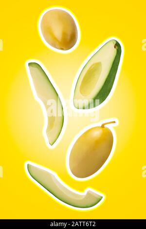 Falling green pickled olives and avocado isolated on yellow background. Stock Photo